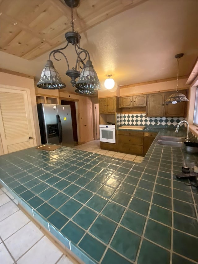 kitchen featuring tile counters, a sink, tile patterned flooring, oven, and stainless steel fridge with ice dispenser