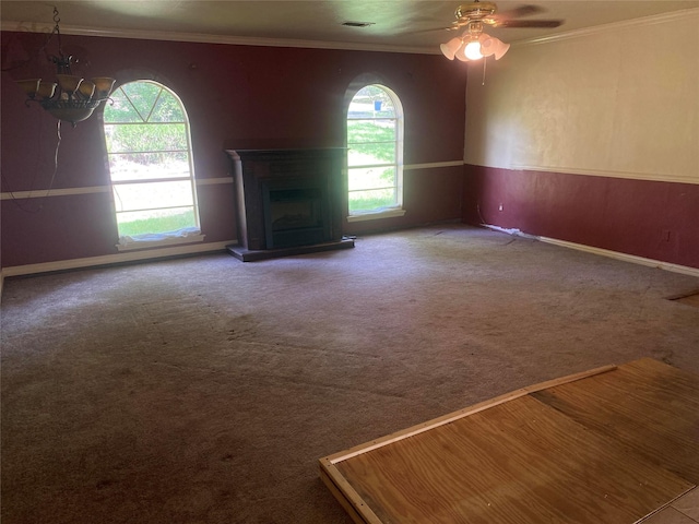 unfurnished living room featuring a fireplace with raised hearth, ceiling fan with notable chandelier, carpet floors, visible vents, and ornamental molding