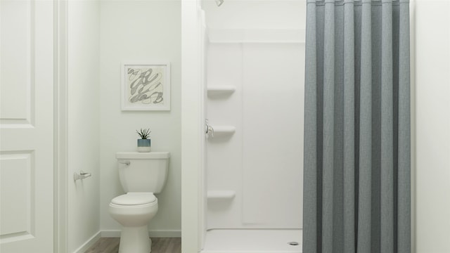 bathroom featuring wood finished floors, a shower stall, toilet, and baseboards