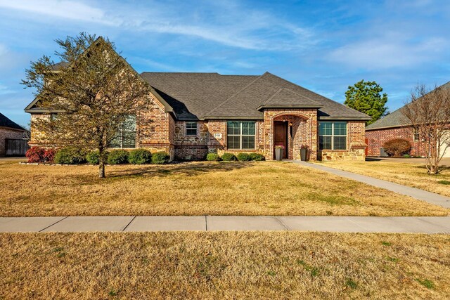 view of front of property with brick siding, a front lawn, and a shingled roof