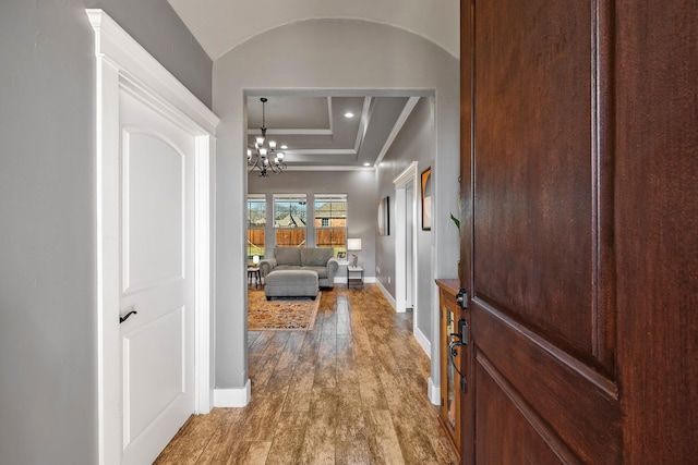 hallway featuring baseboards, lofted ceiling, ornamental molding, wood finished floors, and a chandelier