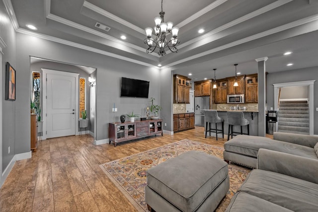 living area with crown molding, light wood finished floors, a raised ceiling, visible vents, and a chandelier