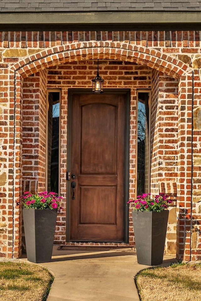 doorway to property featuring brick siding and roof with shingles