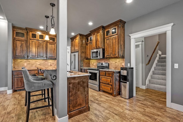 kitchen featuring light wood-style flooring, stainless steel appliances, a kitchen breakfast bar, backsplash, and glass insert cabinets