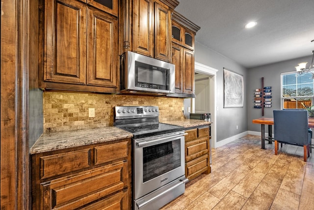 kitchen featuring baseboards, glass insert cabinets, backsplash, stainless steel appliances, and a notable chandelier