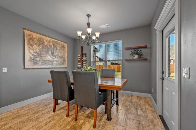 dining room with visible vents, baseboards, a healthy amount of sunlight, light wood finished floors, and an inviting chandelier