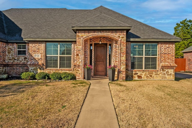 view of front of home with brick siding, roof with shingles, and a front yard