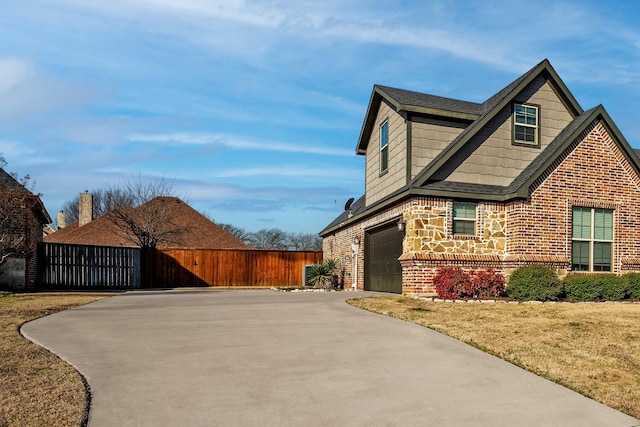 view of side of property with brick siding, fence, a garage, stone siding, and driveway