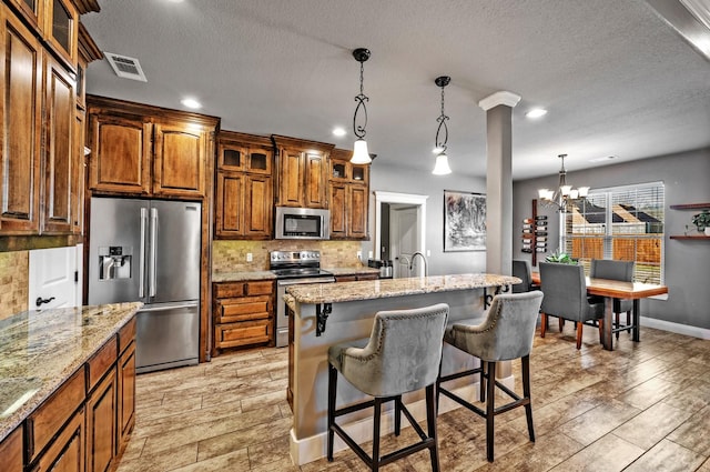 kitchen with a breakfast bar, brown cabinetry, stainless steel appliances, backsplash, and visible vents