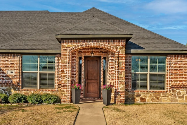 property entrance with stone siding, brick siding, and roof with shingles