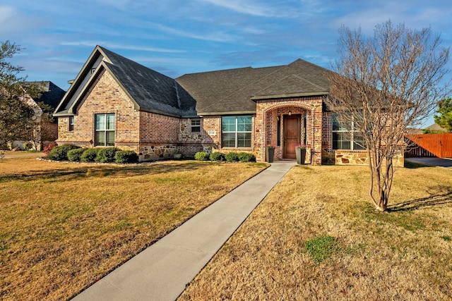 view of front facade featuring a shingled roof, a front yard, fence, and brick siding