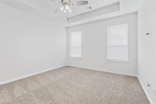 carpeted empty room featuring a ceiling fan, a tray ceiling, visible vents, and baseboards