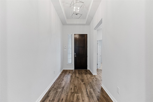 entrance foyer with baseboards, dark wood finished floors, a tray ceiling, and a chandelier