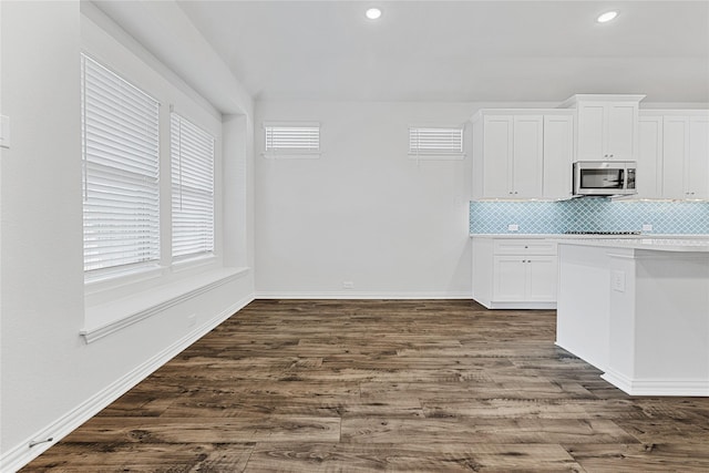 kitchen featuring white cabinets, stainless steel microwave, dark wood finished floors, and decorative backsplash