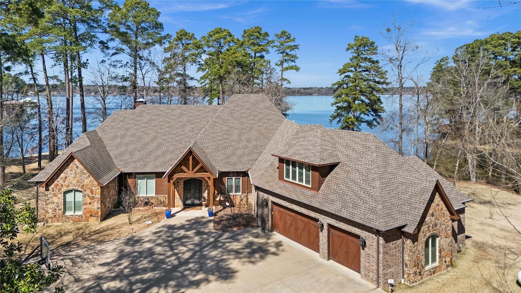 view of front facade featuring a garage, stone siding, a water view, and concrete driveway