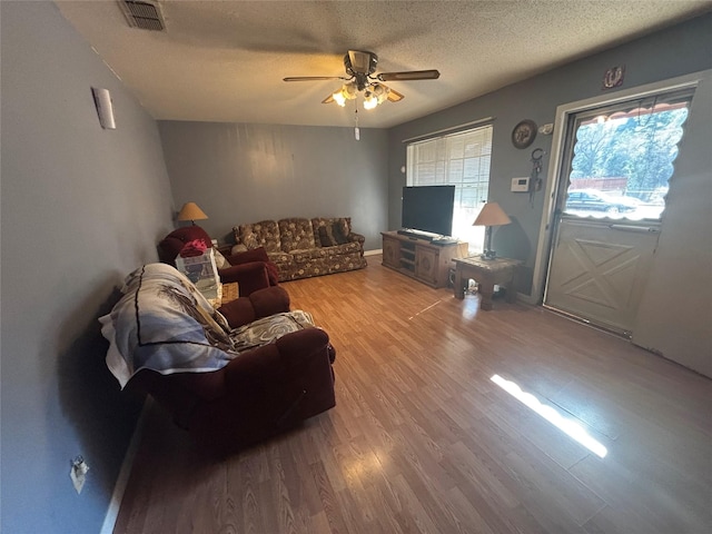 living room featuring ceiling fan, a textured ceiling, visible vents, and wood finished floors