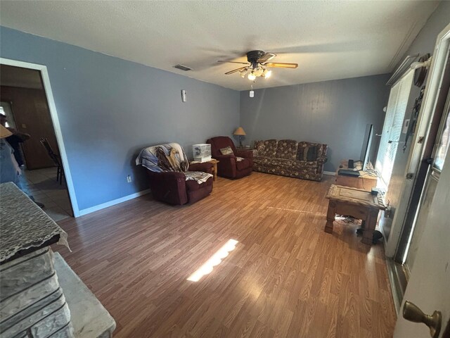 living room featuring wood finished floors, a textured ceiling, ceiling fan, baseboards, and visible vents