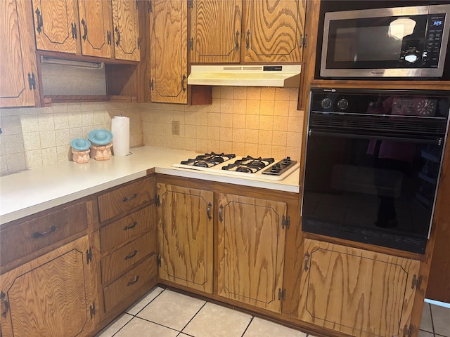 kitchen featuring white gas stovetop, stainless steel microwave, light tile patterned flooring, oven, and under cabinet range hood