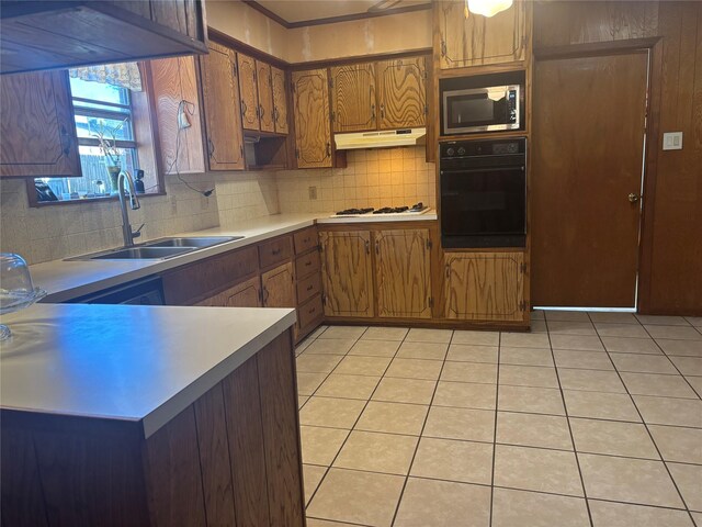 kitchen with a sink, light countertops, stainless steel microwave, under cabinet range hood, and black oven