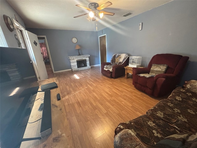 living area with a stone fireplace, wood finished floors, ceiling fan, baseboards, and visible vents