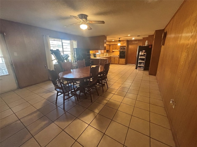dining space with a textured ceiling, a ceiling fan, wood walls, and light tile patterned floors