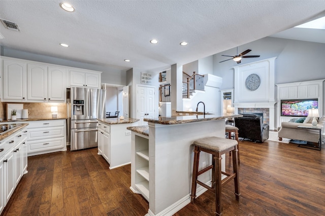 kitchen featuring a tile fireplace, a kitchen island with sink, visible vents, open floor plan, and stainless steel refrigerator with ice dispenser