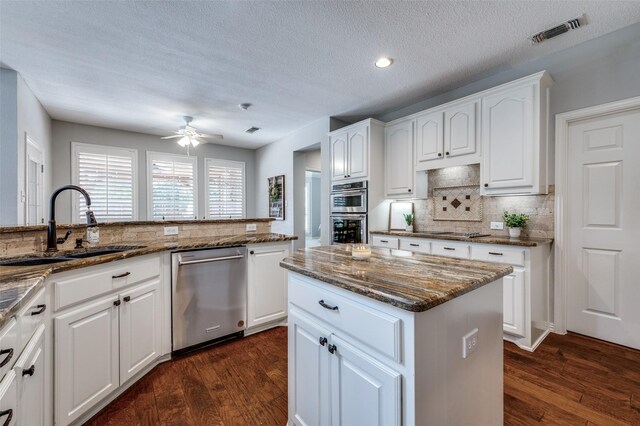 kitchen with a sink, visible vents, appliances with stainless steel finishes, dark stone countertops, and dark wood finished floors