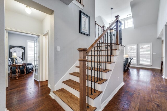 stairway with hardwood / wood-style floors, a towering ceiling, and baseboards