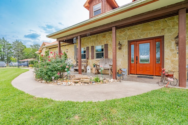 doorway to property featuring covered porch, stone siding, and a lawn