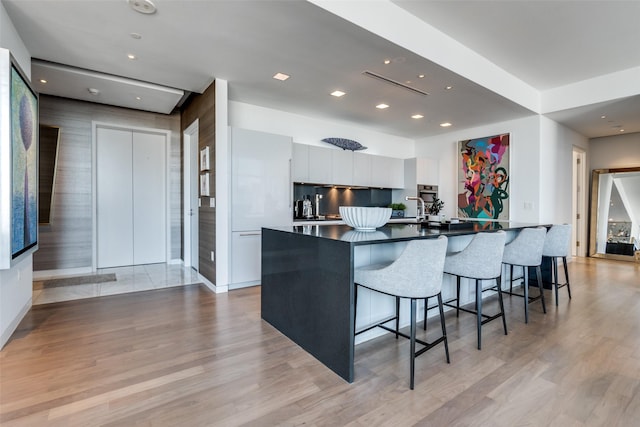 kitchen featuring light wood finished floors, a breakfast bar area, dark countertops, white cabinets, and modern cabinets