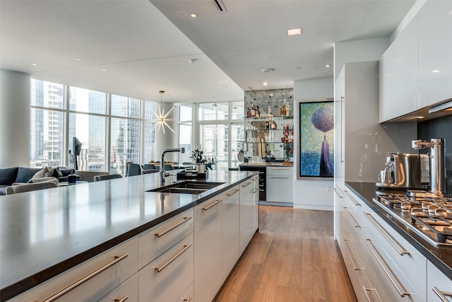 kitchen with stainless steel gas cooktop, light wood finished floors, open floor plan, white cabinetry, and a sink