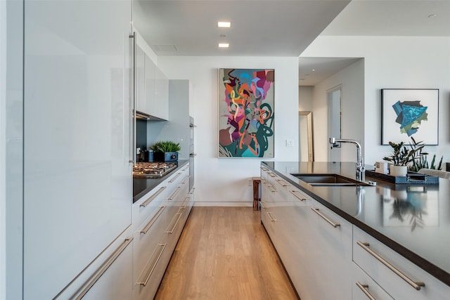 kitchen with dark countertops, light wood-style flooring, white cabinets, a sink, and modern cabinets