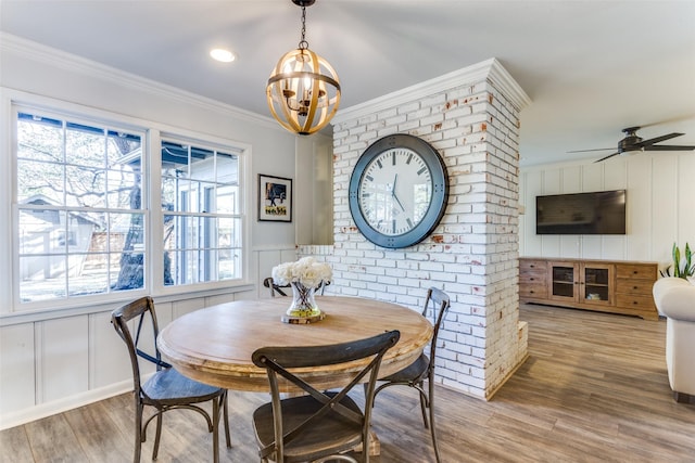 dining room with ceiling fan with notable chandelier, a decorative wall, wood finished floors, and crown molding