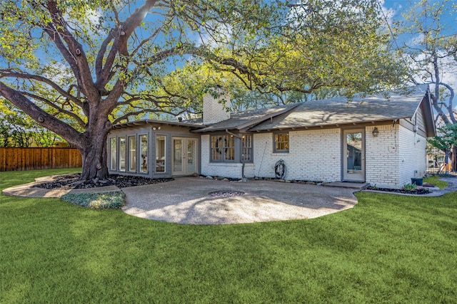 back of property featuring brick siding, fence, a yard, french doors, and a chimney