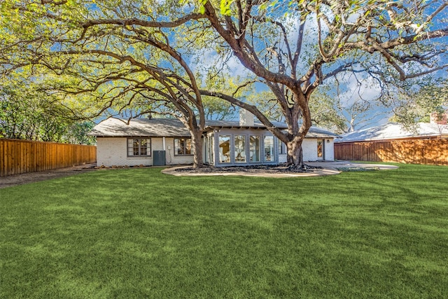 back of property featuring brick siding, a fenced backyard, central AC, and a yard