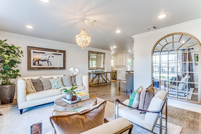 living room featuring crown molding, visible vents, a notable chandelier, and wood finished floors