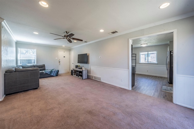 living room featuring carpet, visible vents, crown molding, and wainscoting