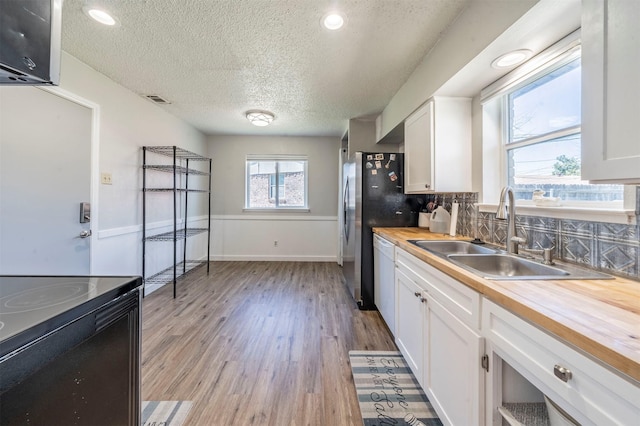 kitchen with butcher block countertops, visible vents, white cabinets, and a sink