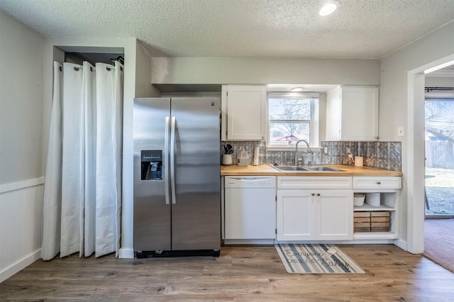 kitchen featuring white cabinets, a sink, wood finished floors, stainless steel fridge, and dishwasher