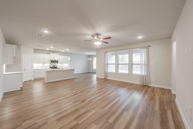 unfurnished living room featuring recessed lighting, visible vents, light wood-style flooring, and ceiling fan with notable chandelier