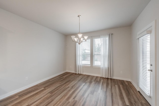 unfurnished room featuring a notable chandelier, baseboards, and wood finished floors