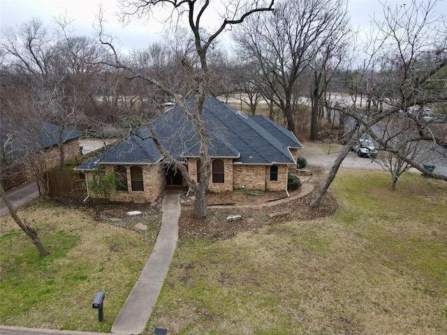 view of front of property featuring driveway, brick siding, a front lawn, and roof with shingles