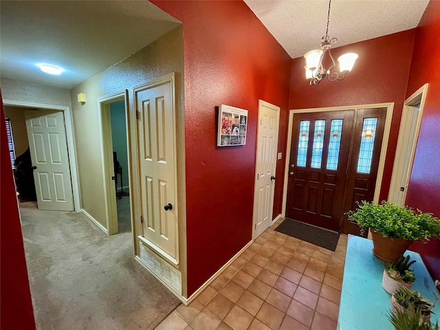 entrance foyer featuring a textured ceiling, a textured wall, a chandelier, baseboards, and vaulted ceiling