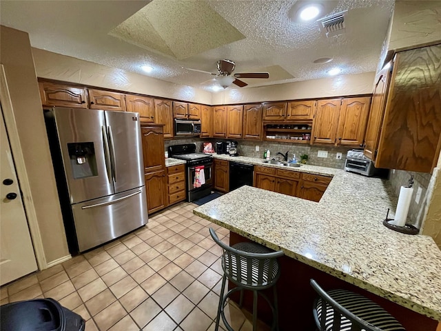 kitchen featuring stainless steel appliances, tasteful backsplash, brown cabinetry, a sink, and a peninsula