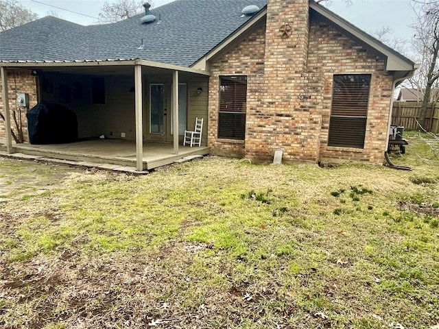 rear view of house with roof with shingles, fence, a lawn, and brick siding