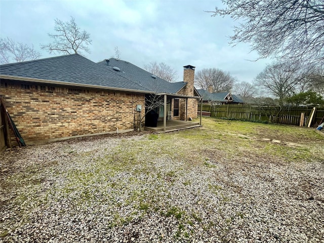 back of house with brick siding, fence, roof with shingles, a lawn, and a chimney