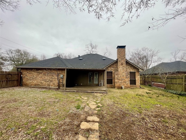 rear view of property featuring brick siding, fence, a chimney, and a lawn