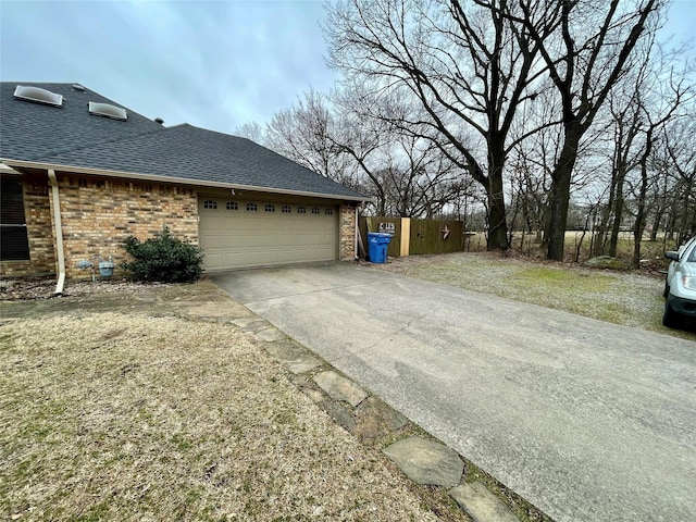 view of property exterior featuring concrete driveway, roof with shingles, an attached garage, a gate, and brick siding