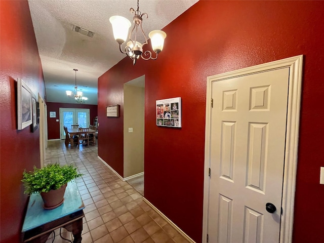 corridor featuring a textured ceiling, visible vents, baseboards, tile patterned floors, and an inviting chandelier