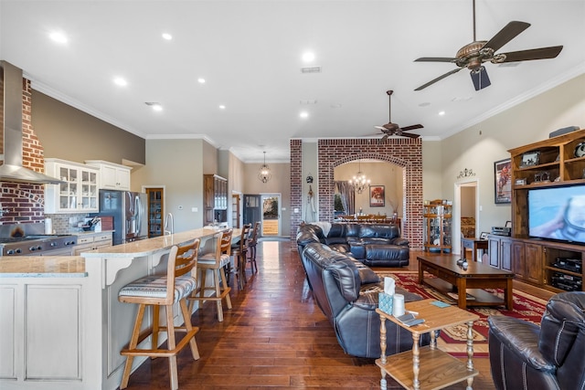 living room with visible vents, arched walkways, dark wood-style floors, ornamental molding, and ceiling fan with notable chandelier